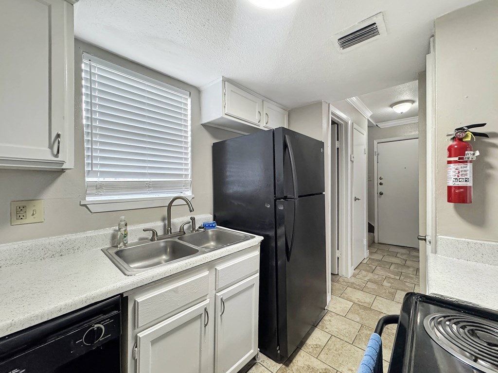 A black refrigerator sits in a kitchen with white cabinets and a black dishwasher.