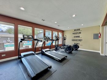 A gym with treadmills and a wall with the words "Believe Discipline Strong Consistency Secret" written on it.