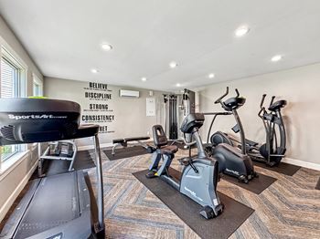 A gym with a treadmill, elliptical machines, and a wall with motivational words.