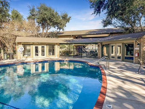 A swimming pool in front of a house with a patio.
