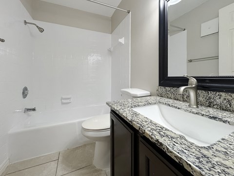 Bathroom with granite vanity, mirror, and tub-shower combo at Los Cedros Apartments