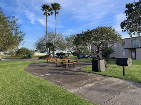 Picnic area with tables, grill, and shade trees at Los Cedros Apartments