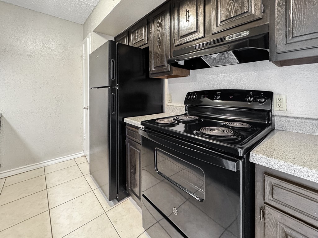 Compact kitchen with black appliances and white tile floor – Borders Apartments Brownsville TX