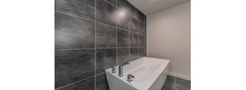 A white sink with chrome faucets in a bathroom with grey tiles.