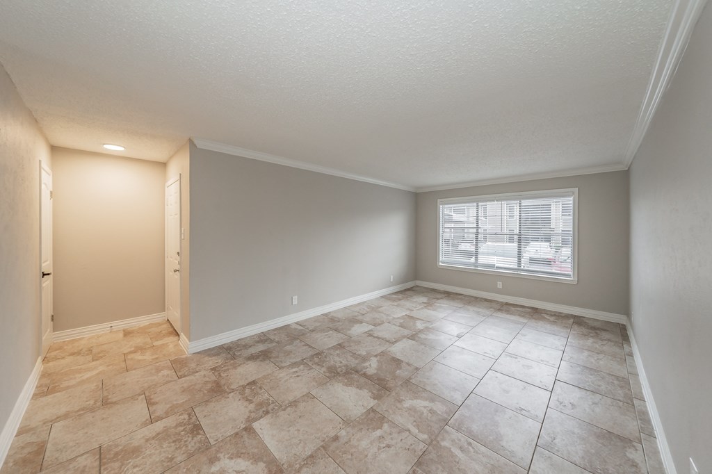 Open-concept living room with neutral tones and tile floors at Riata Park Apartments