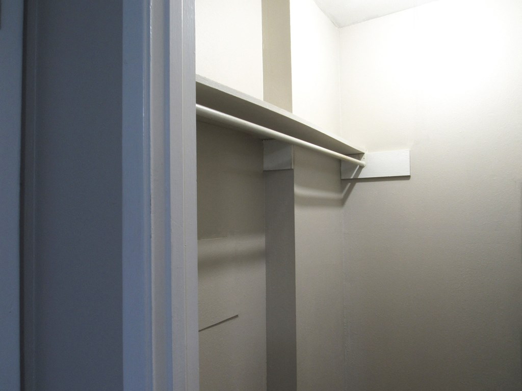 a walk in closet with a white wall and a white closet door with a shelf