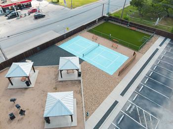 A tennis court is surrounded by parking spaces and a small grassy area.