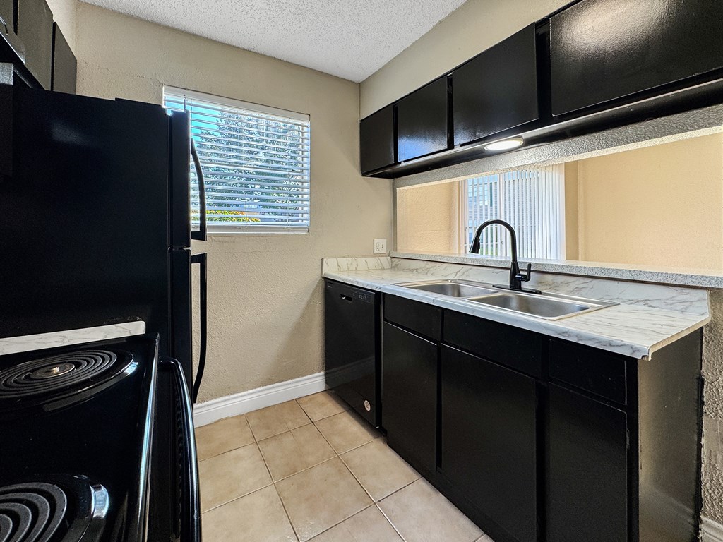 A black fridge is in a kitchen with black cabinets and a white sink.