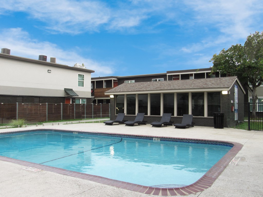 a swimming pool in front of a building with lounge chairs