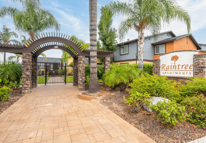 A brick pathway leads to a gate with an archway and a sign that says Raintree Apartments at Raintree Apartments, CA 92346
