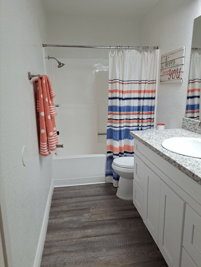 A white bathroom with a towel hanging on the wall at Raintree Apartments, CA 92346