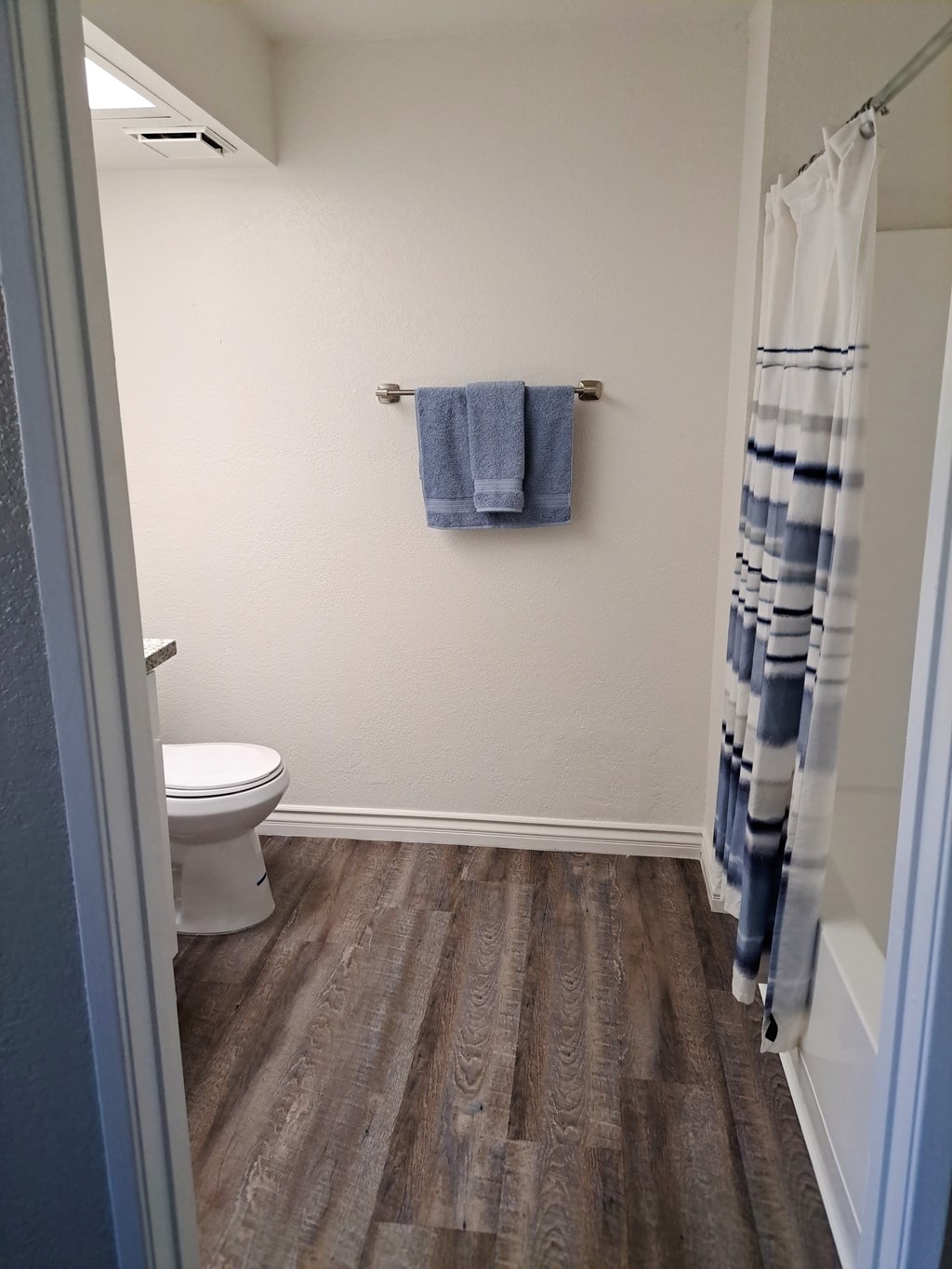 A bathroom with a toilet, a towel, and a shower curtain at Raintree Apartments, CA 92346