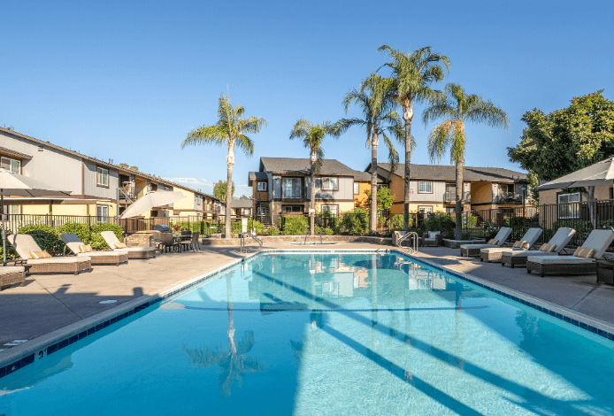 A swimming pool surrounded by palm trees and lounge chairs at Raintree Apartments, CA 92346
