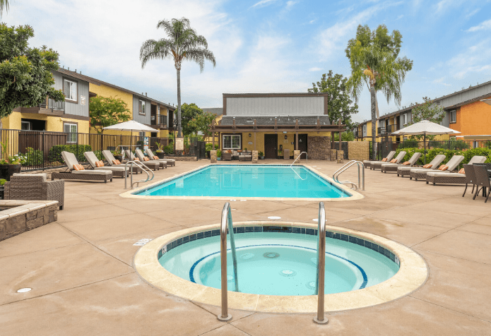 A large outdoor swimming pool surrounded by sun loungers and palm trees at Raintree Apartments, CA 92346