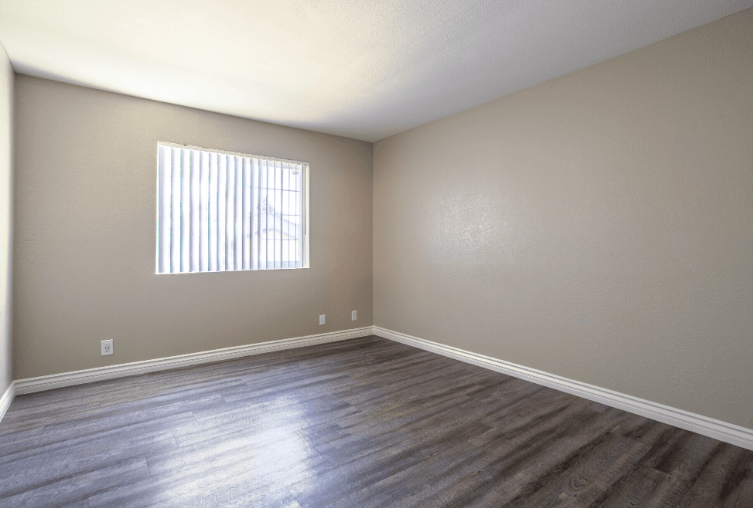 A room with wooden flooring and a window with blinds at Raintree Apartments, CA 92346