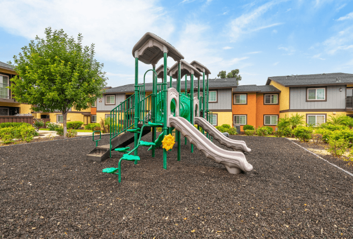 A playground with a green slide and a yellow flower at Raintree Apartments, CA 92346