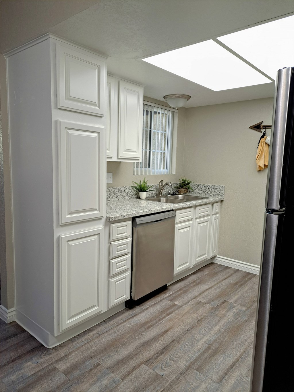 A kitchen with white cabinets and a stainless steel refrigerator at Raintree Apartments, CA 92346