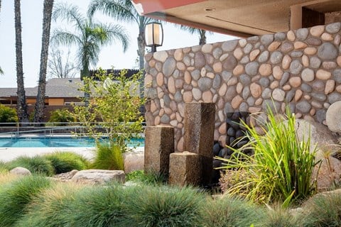 a water fountain in front of a stone wall next to a swimming pool
