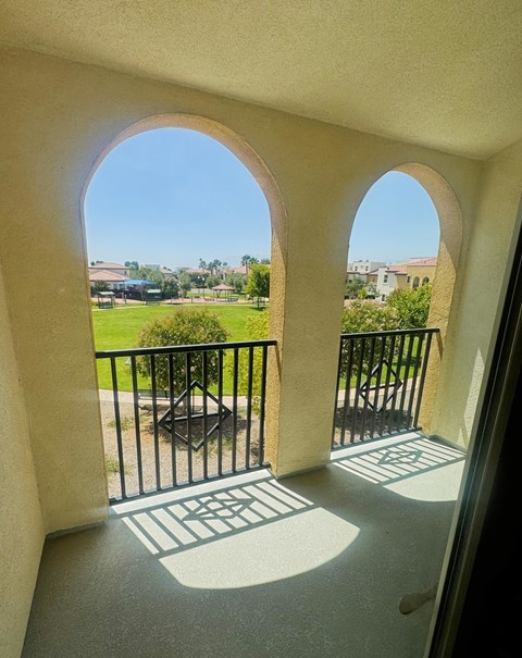 A balcony with a black railing and a view of a green lawn and buildings.