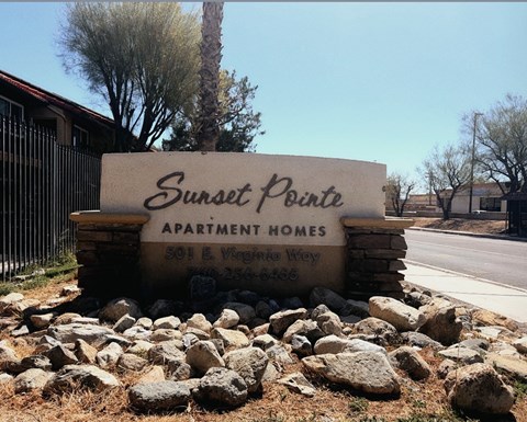 A sign for Sunset Pointe Apartment Homes sits in front of a fence and trees.