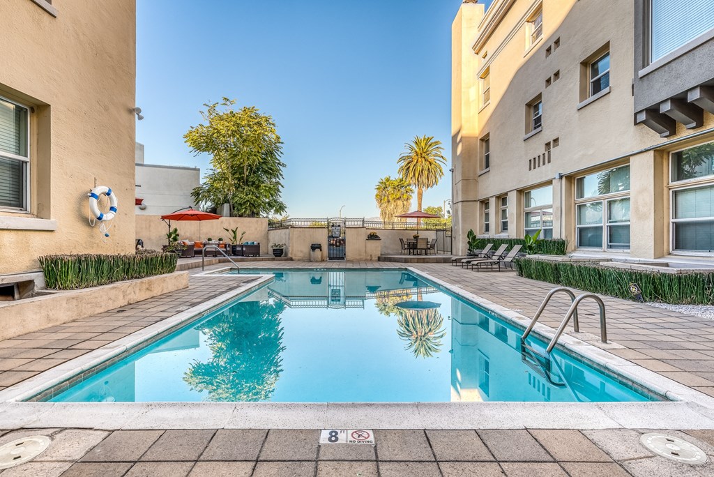 a swimming pool with a yellow building and palm trees in the background