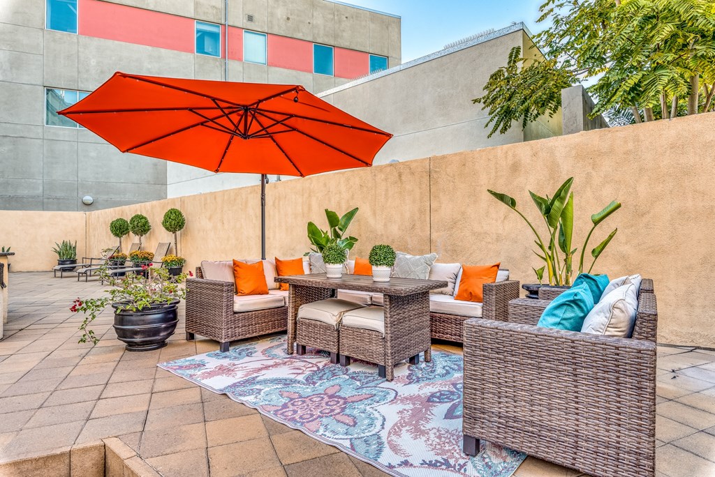 a patio with wicker furniture and an orange umbrella