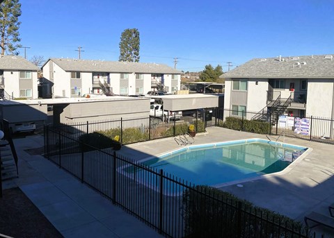 A pool surrounded by a black fence in front of apartment buildings.