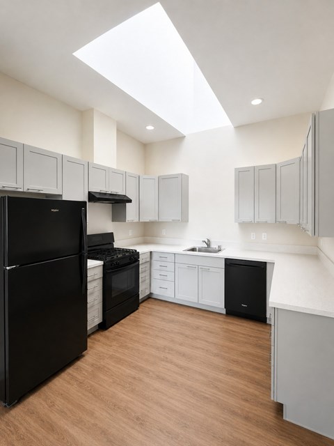 A black refrigerator is in a kitchen with wooden floors and white walls.