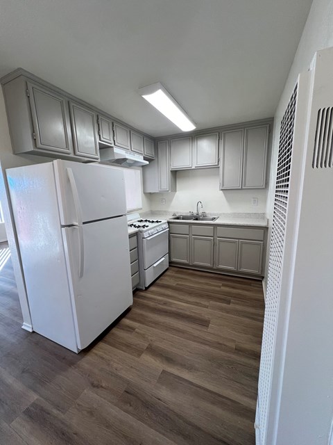 A white refrigerator is in a kitchen with wooden floors.