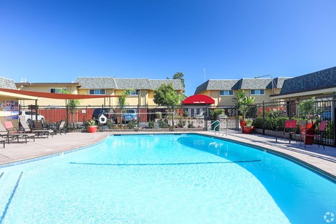 A large swimming pool in front of a building with a red umbrella.