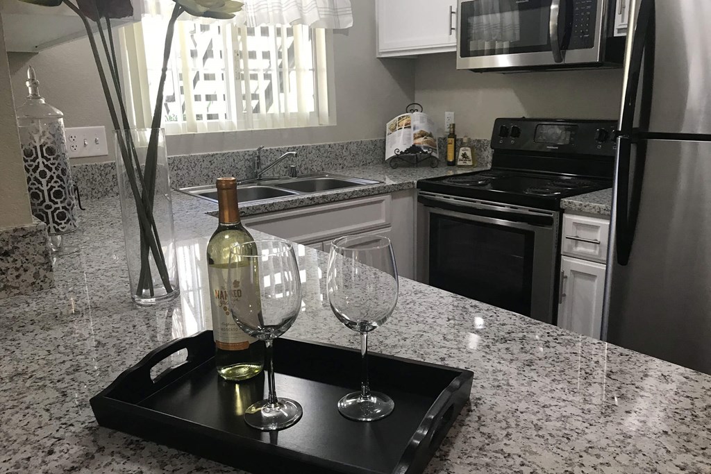 a kitchen with granite countertops and a black tray with a bottle of wine and two glasses
