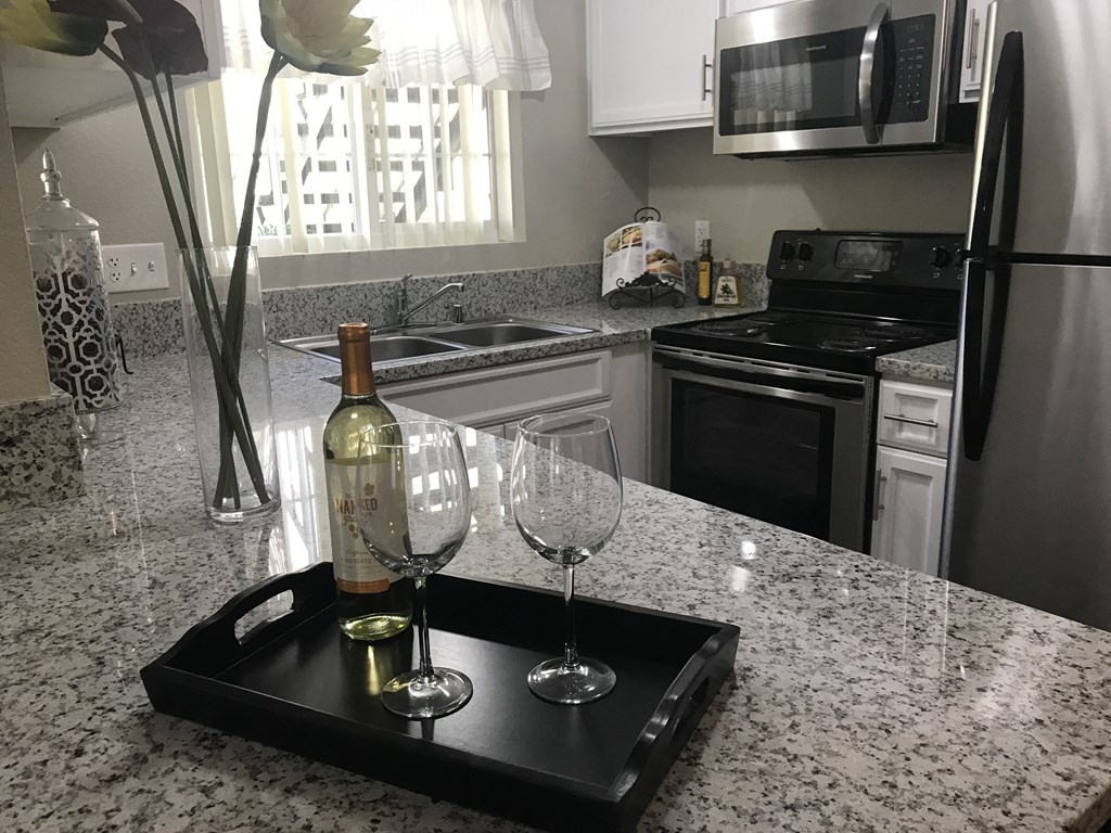 a kitchen with granite countertops and a black tray with a bottle of wine and two glasses