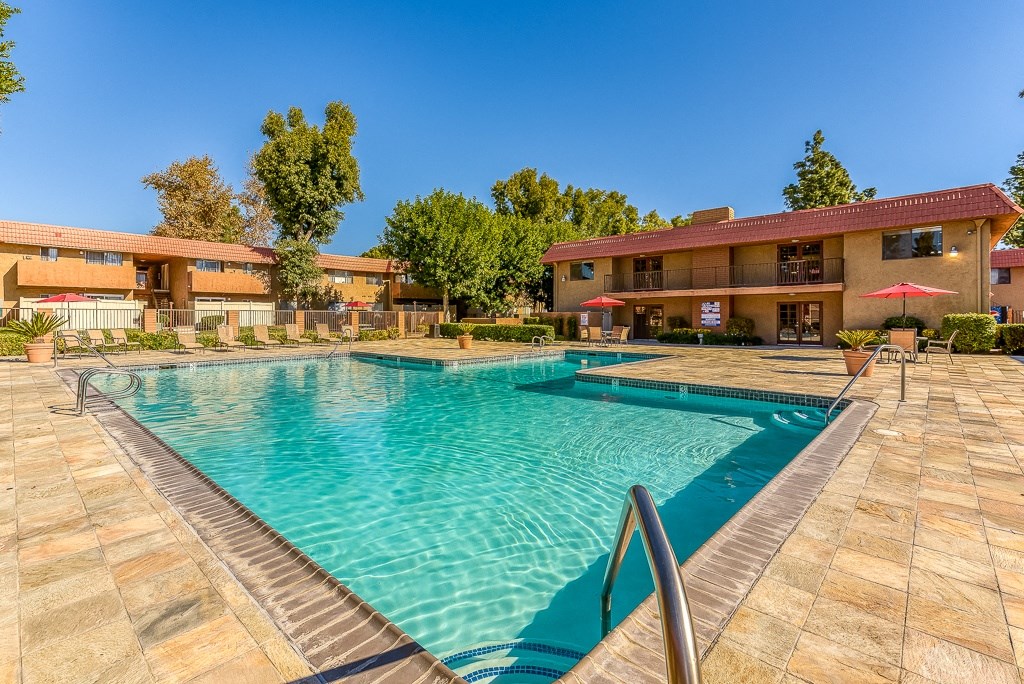 A swimming pool in front of a building with a red umbrella.