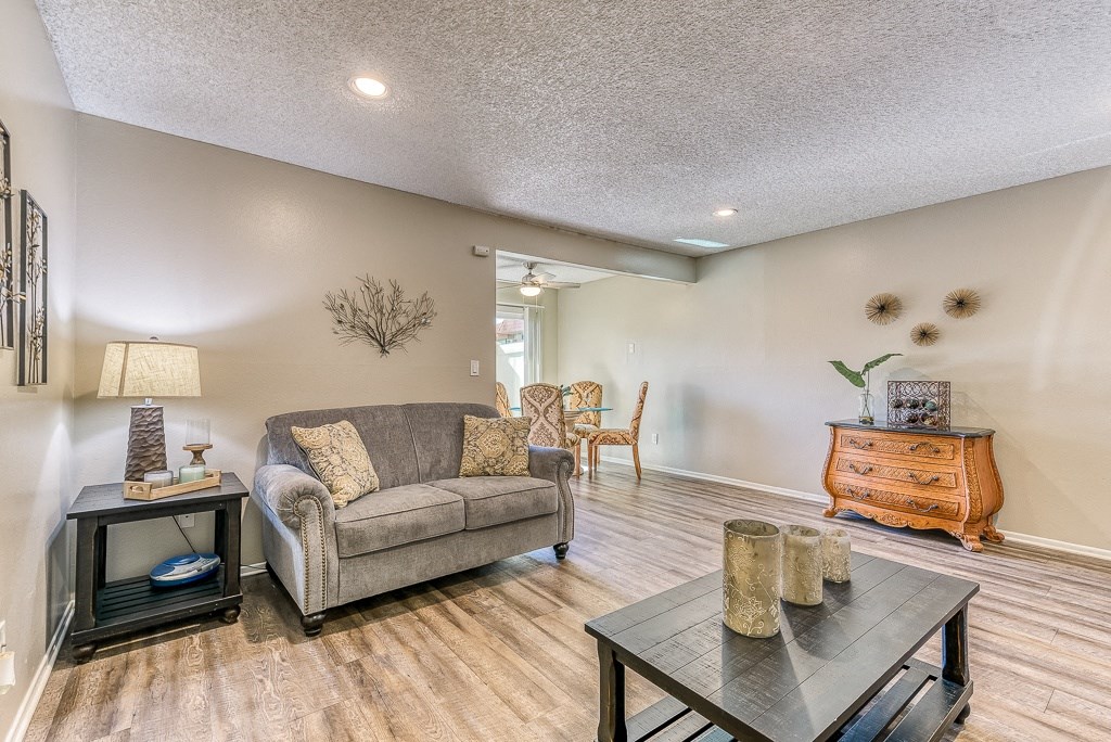 A living room with a grey couch, a wooden coffee table, and a wooden side table with a lamp.