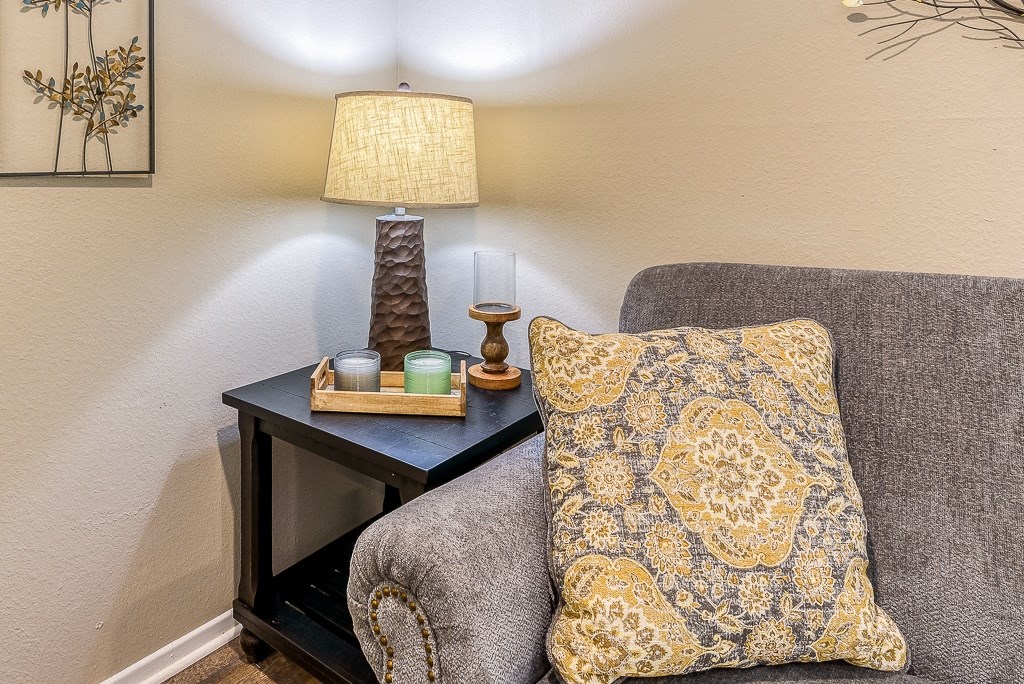 A grey couch with a yellow and white pillow sits next to a table with a lamp and candle.