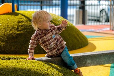 A young child in a plaid shirt and blue jeans is playing on a playground.