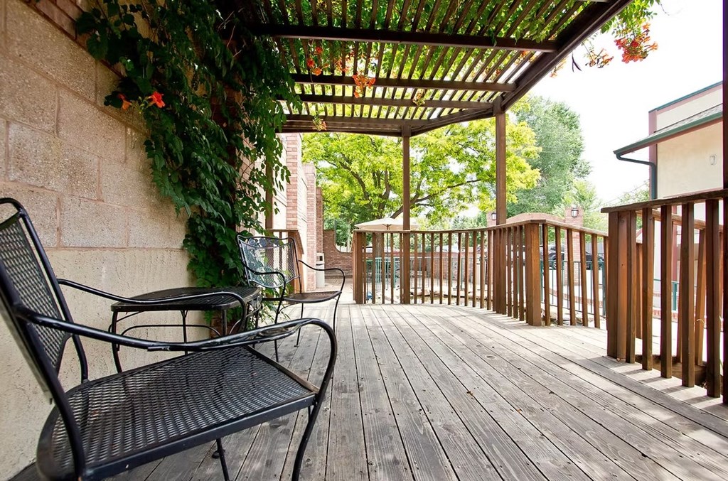 A black metal bench sits on a wooden deck under a pergola.