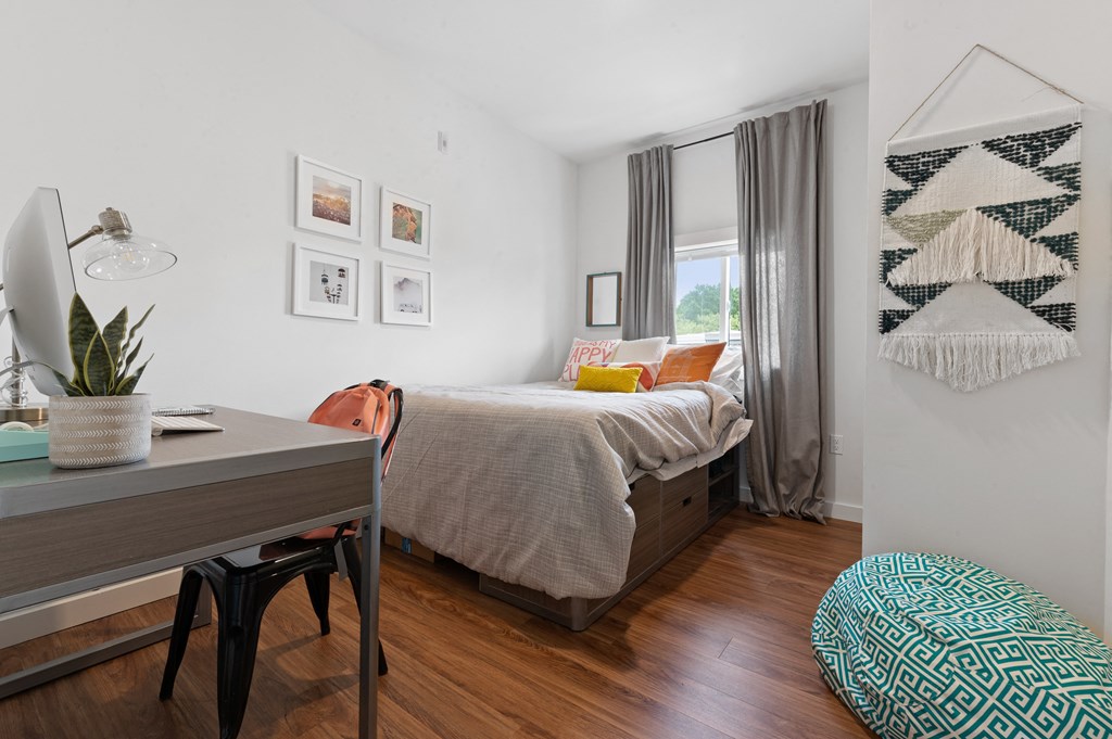 Apartment bedroom furnished for student with full-size platform bed, desk and chair, and a large window