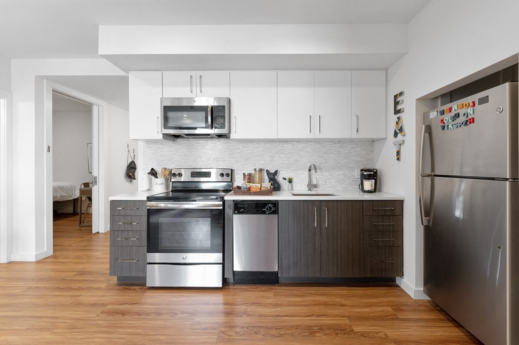 Open student apartment kitchen with two-tone cabinets, stainless steel appliances, and hardwood flooring