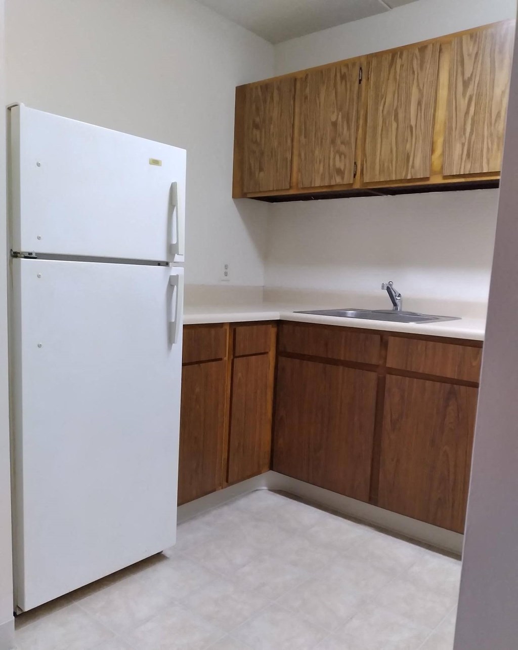 an empty kitchen with a white refrigerator and wooden cabinets