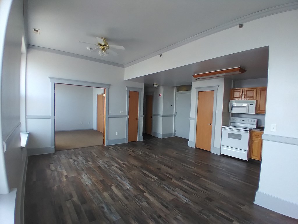 an empty living room with wooden floors and a kitchen