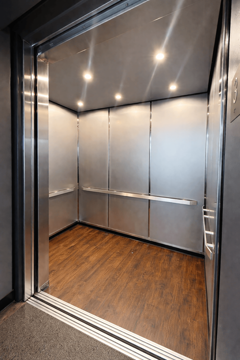 A stainless steel elevator with a glass door and wood flooring inside.