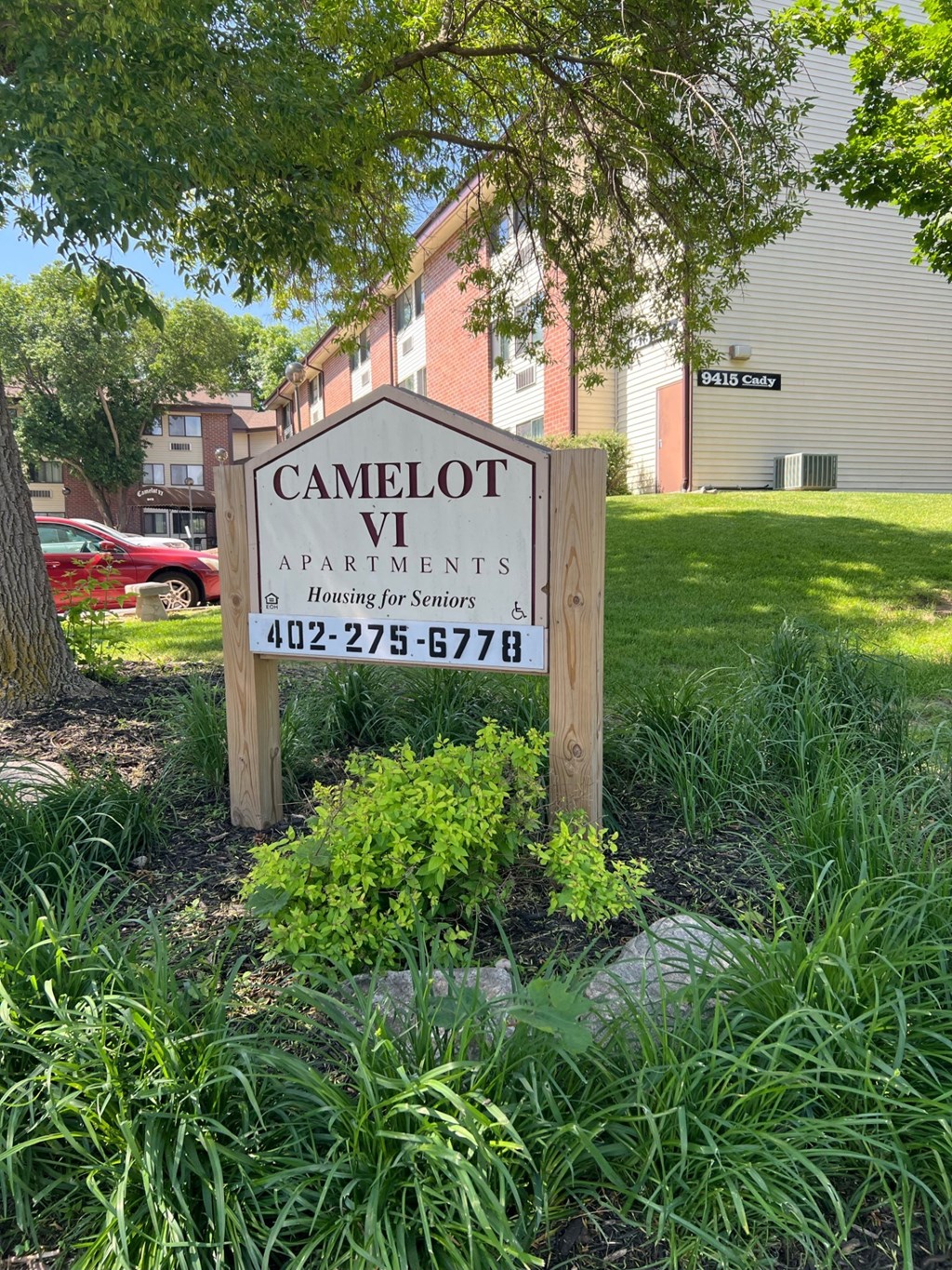 A sign for Camelot Apartments is in front of a building.