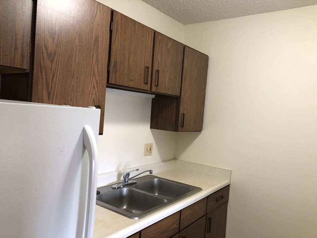 A kitchen with a white fridge and brown cabinets.