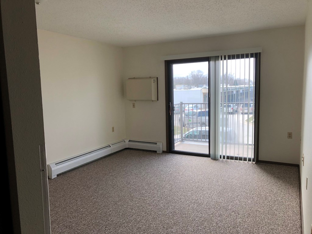 A room with a carpeted floor, a window with blinds, and a sliding glass door.