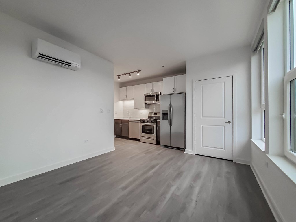 an empty living room with a white door and a kitchen