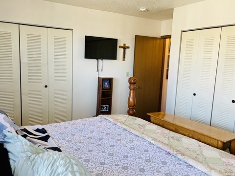 A bedroom with a bed, a TV, and a cross on the wall.