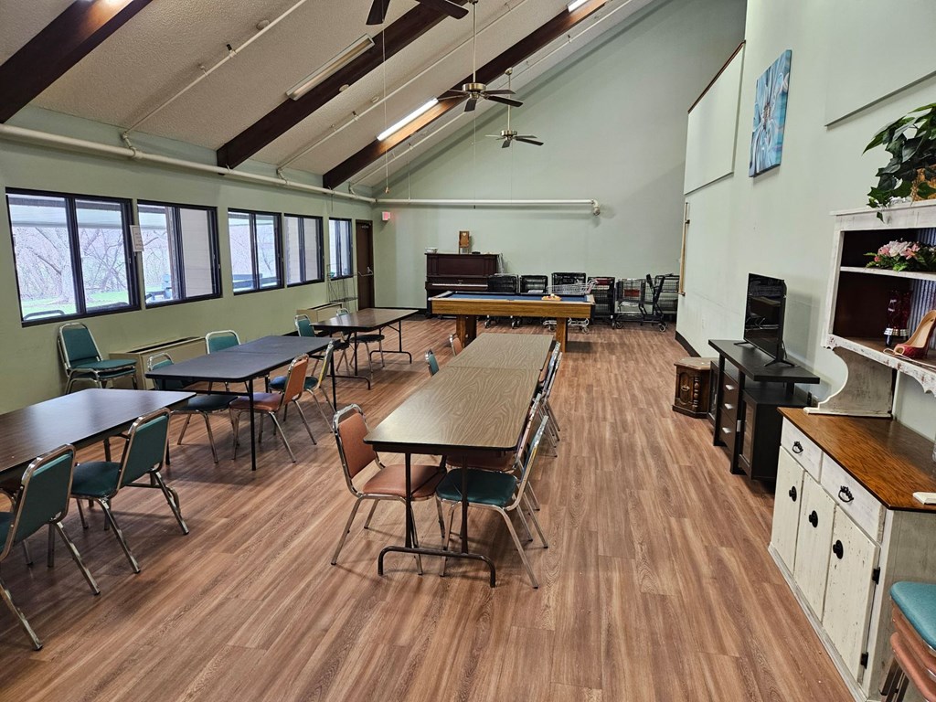 A room with wooden floors and a variety of furniture including chairs, tables, and a kitchenette.