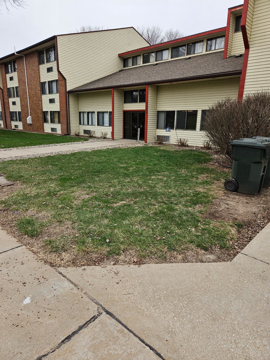 A grassy area in front of a building with a trash can to the side.