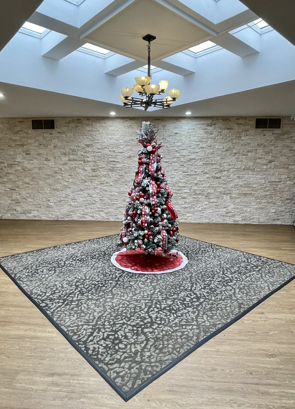 A Christmas tree is placed on a round table in a room with a chandelier.